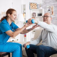 senior-man-nursing-home-with-doing-physical-therapy-with-help-from-nurse-using-dumbbells-min-min